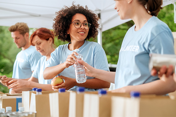 a woman standing in a line with other volunteers doing charitable giving- putting water in paper bags