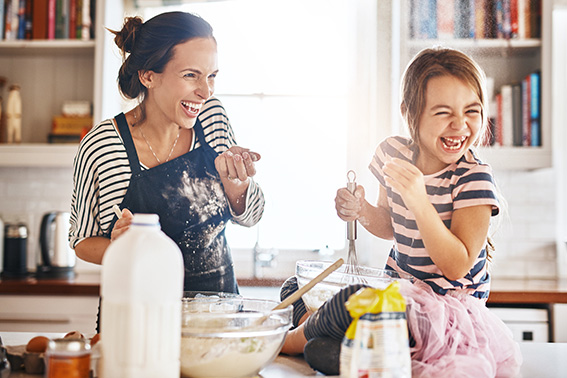 woman and girl laughing as they cook in the kitchen and practicing smart saving by cooking their own food.