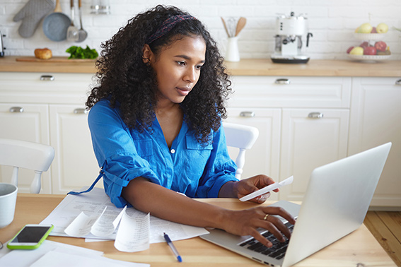 A woman sitting at a table, looking at a laptop, starting the 2024 tax season.