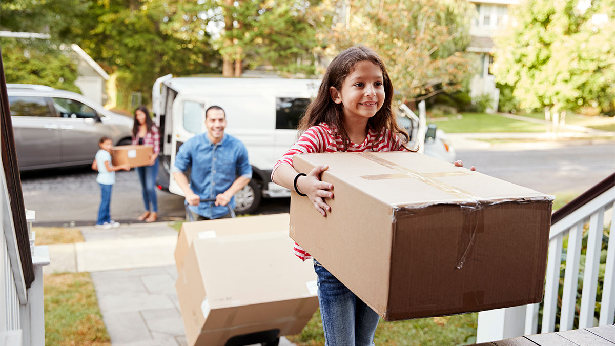 family bringing boxes up outdoor stairs into suburban home for a blog about The Advantages of Buying a House vs. Renting