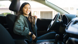 Young adult putting on seatbelt in drivers seat of car for a blog about How to Get Approved for a First-Time Car Buyer Loan